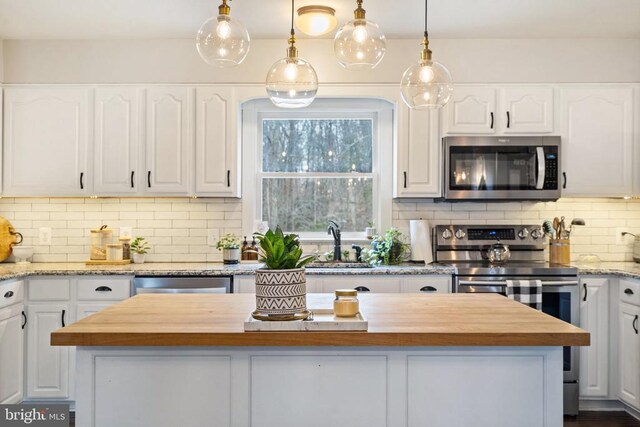 kitchen with stainless steel appliances, white cabinetry, a kitchen island, and butcher block counters