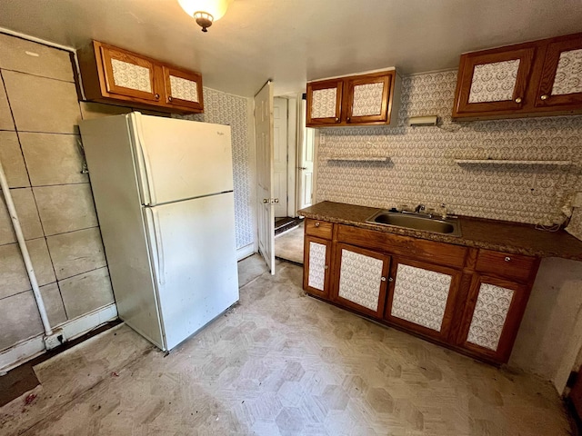 kitchen with freestanding refrigerator, a sink, dark countertops, and brown cabinets