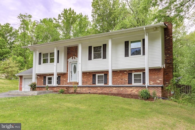 split foyer home with a chimney, driveway, brick siding, a garage, and a front yard