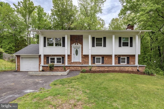 raised ranch featuring a front yard, a garage, a chimney, and driveway