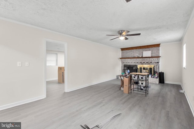 living area with crown molding, wood finished floors, a fireplace, a textured ceiling, and a ceiling fan