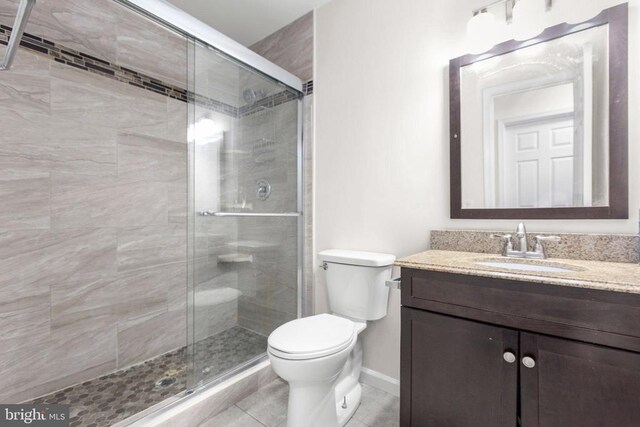 bathroom with a shower stall, toilet, vanity, and baseboards