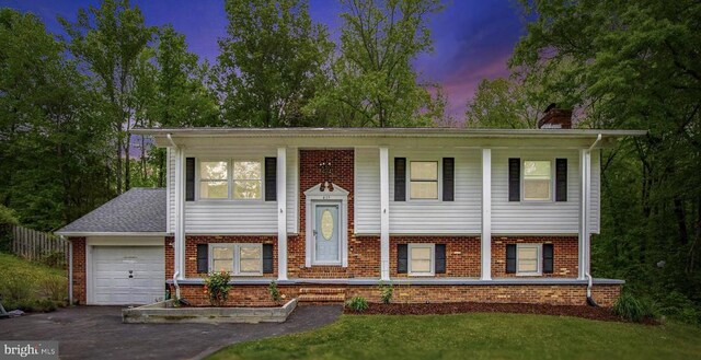 split foyer home with a chimney, driveway, brick siding, covered porch, and an attached garage