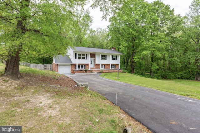split foyer home featuring a chimney, fence, aphalt driveway, a front yard, and brick siding