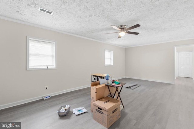 empty room featuring wood finished floors, ceiling fan, crown molding, baseboards, and a textured ceiling