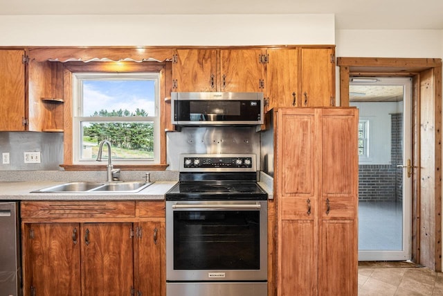kitchen with appliances with stainless steel finishes, a sink, healthy amount of natural light, and brown cabinets