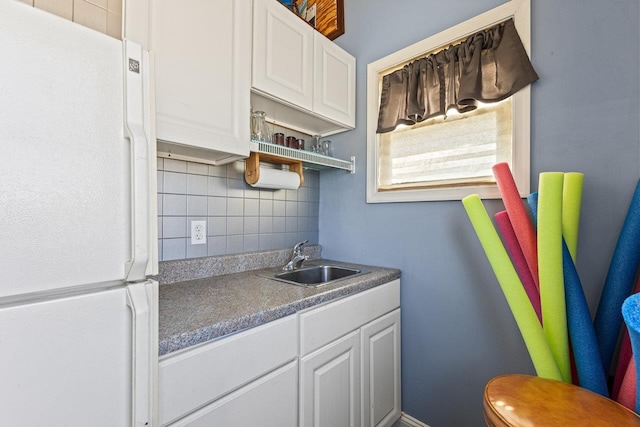 kitchen featuring freestanding refrigerator, a sink, decorative backsplash, and white cabinets