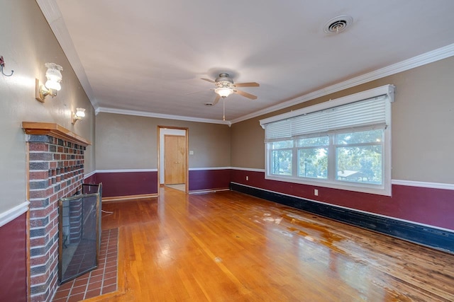unfurnished living room featuring a ceiling fan, wood finished floors, a brick fireplace, baseboards, and ornamental molding