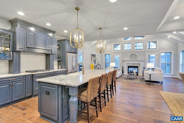 kitchen featuring gray cabinets, a breakfast bar, stainless steel appliances, light stone countertops, and a center island with sink