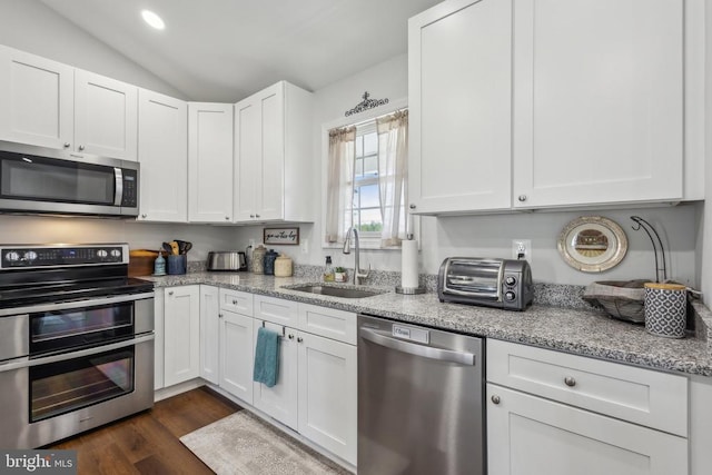 kitchen featuring stainless steel appliances, a sink, white cabinetry, vaulted ceiling, and light stone countertops