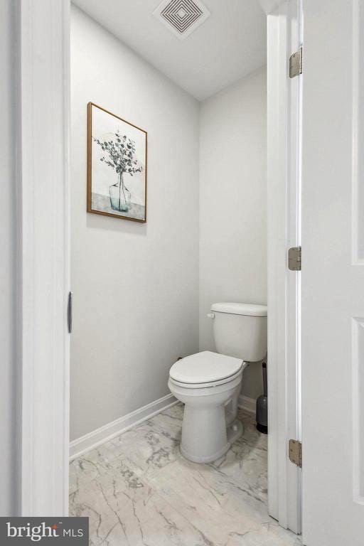 bathroom with marble look tile flooring, toilet, and baseboards