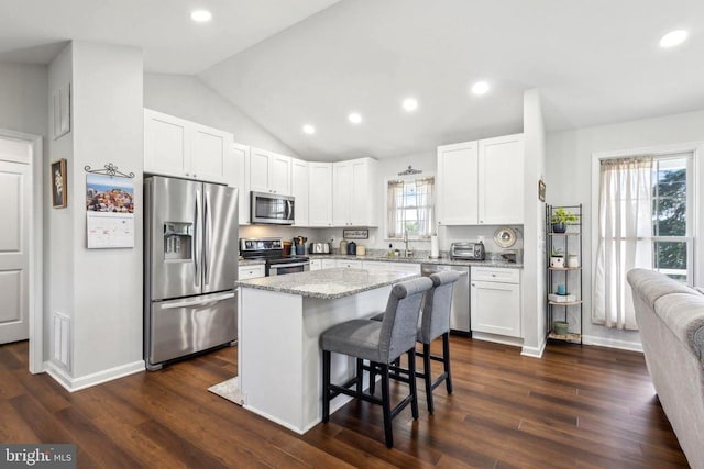 kitchen featuring stainless steel appliances, a center island, a breakfast bar, vaulted ceiling, and white cabinetry