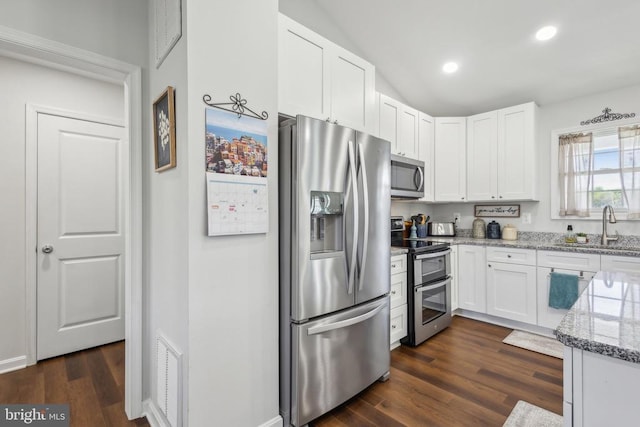 kitchen with appliances with stainless steel finishes, a sink, white cabinetry, light stone counters, and dark wood finished floors