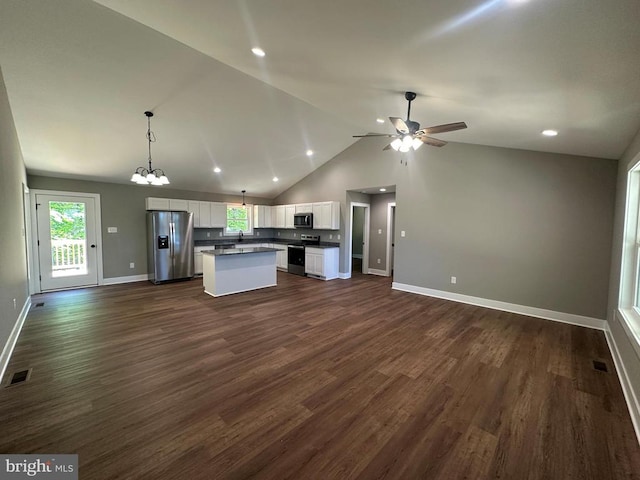 kitchen with appliances with stainless steel finishes, open floor plan, dark countertops, white cabinetry, and a center island