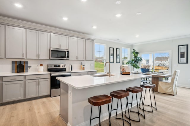 kitchen with stainless steel appliances, a sink, gray cabinetry, ornamental molding, and light wood-style flooring