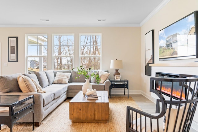 living area featuring light wood-style floors, crown molding, baseboards, and a glass covered fireplace