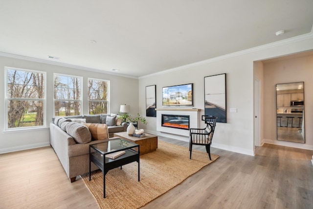 living area with crown molding, a glass covered fireplace, light wood-type flooring, and baseboards