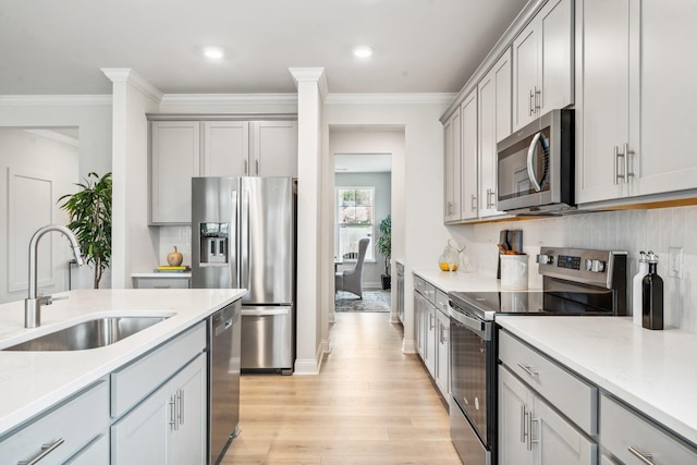 kitchen featuring stainless steel appliances, a sink, gray cabinets, crown molding, and light wood-type flooring