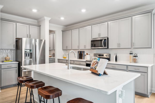 kitchen with appliances with stainless steel finishes, gray cabinets, a sink, a breakfast bar area, and backsplash