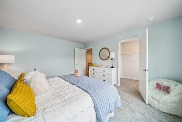 bedroom with light colored carpet, a closet, a walk in closet, and baseboards