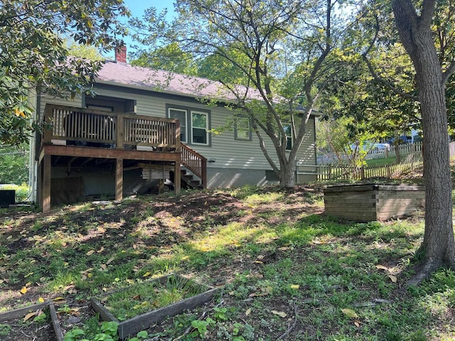 rear view of property with a deck, fence, a chimney, stairway, and a vegetable garden