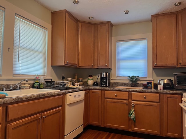 kitchen with white dishwasher, a sink, dark wood-type flooring, range, and dark countertops