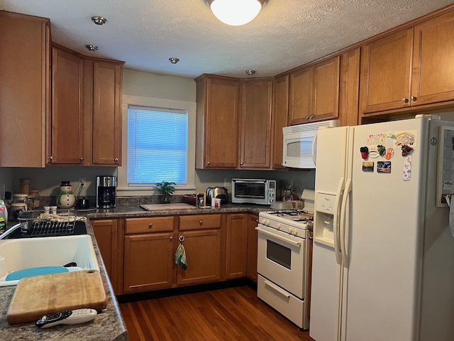 kitchen with white appliances, dark wood-style flooring, brown cabinets, a sink, and a textured ceiling