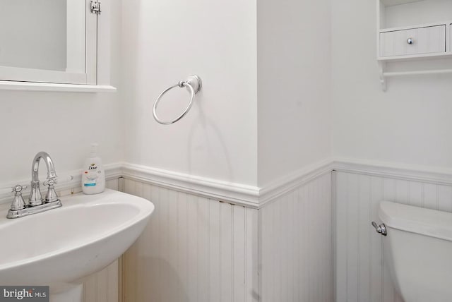 half bath with a sink, wainscoting, toilet, and a decorative wall