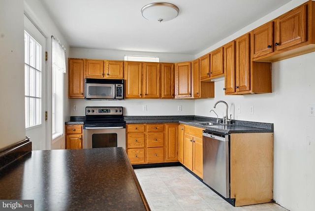 kitchen featuring stainless steel appliances, a sink, dark countertops, and brown cabinets