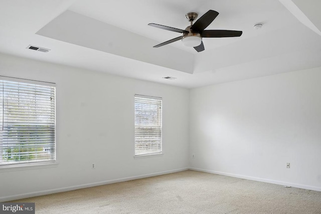 unfurnished room featuring a tray ceiling, ceiling fan, baseboards, and light colored carpet