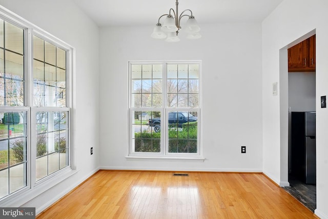 unfurnished dining area featuring a chandelier, light wood finished floors, and healthy amount of natural light