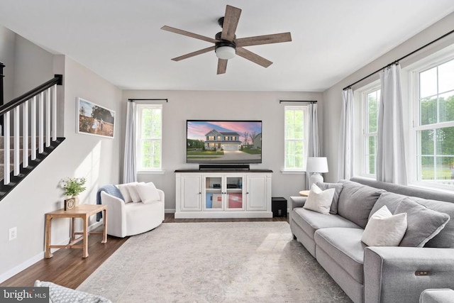 living room featuring wood finished floors, ceiling fan, baseboards, and stairs