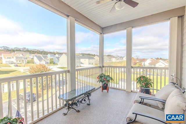 sunroom / solarium featuring a residential view, a ceiling fan, and a healthy amount of sunlight