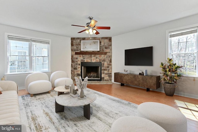 living area with a stone fireplace, wood finished floors, baseboards, and ceiling fan