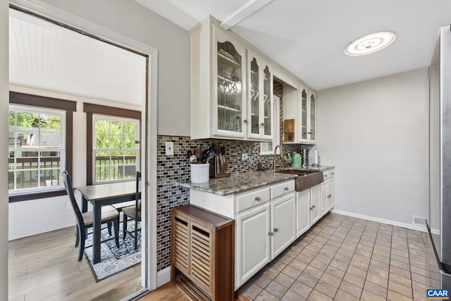 kitchen with a sink, tasteful backsplash, glass insert cabinets, light stone counters, and white cabinets