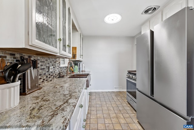 kitchen with stainless steel appliances, backsplash, a sink, glass insert cabinets, and white cabinets