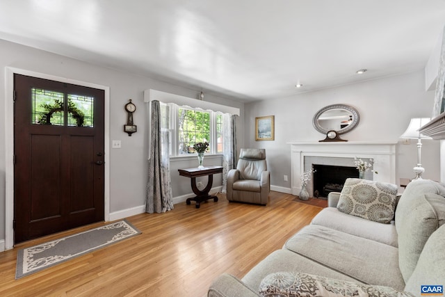 living room featuring light wood-style flooring, a tiled fireplace, and baseboards