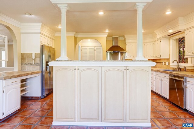 kitchen with a sink, stainless steel appliances, tasteful backsplash, wall chimney range hood, and tile patterned floors