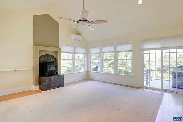 unfurnished living room with a ceiling fan, a wood stove, a wall unit AC, and wood finished floors