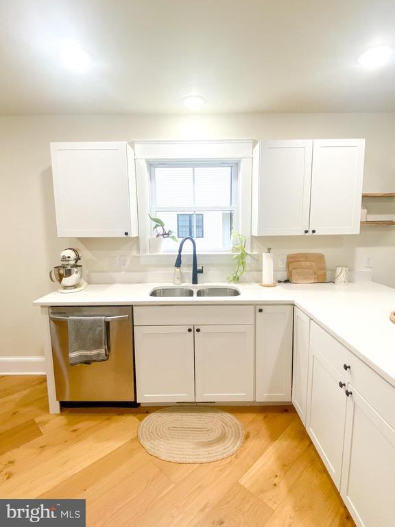 kitchen with white cabinetry, stainless steel dishwasher, sink, and light wood-type flooring