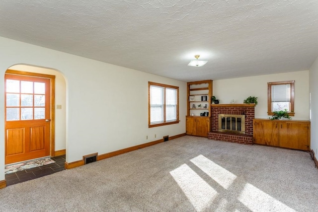 unfurnished living room featuring a textured ceiling, a brick fireplace, and dark colored carpet