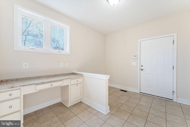 unfurnished office with built in study area, light tile patterned floors, and baseboards