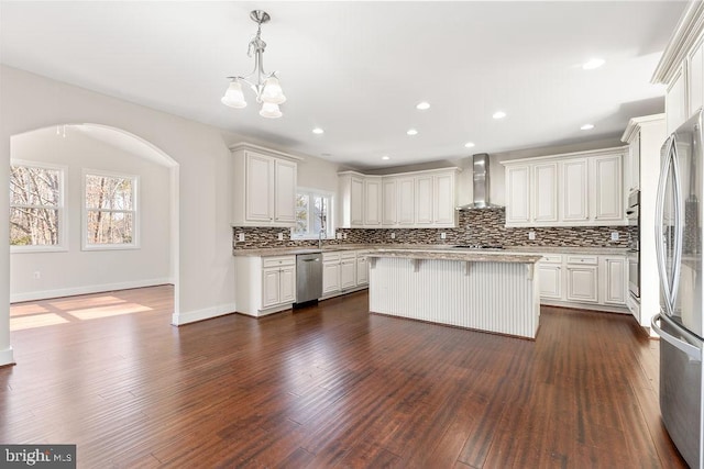 kitchen with stainless steel appliances, wall chimney range hood, backsplash, light countertops, and a chandelier