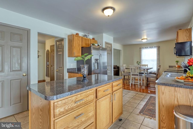 kitchen with stainless steel refrigerator with ice dispenser, light tile patterned flooring, a sink, and dark countertops