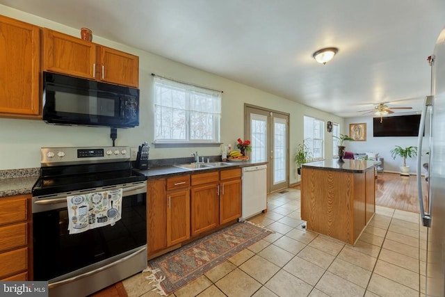 kitchen with appliances with stainless steel finishes, a sink, light tile patterned floors, and brown cabinets