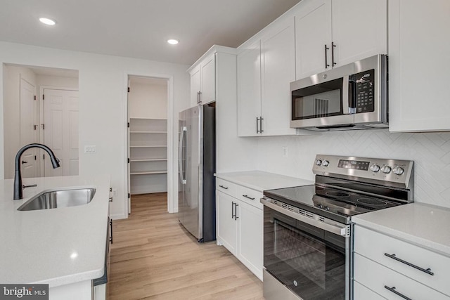 kitchen featuring appliances with stainless steel finishes, a sink, light wood finished floors, white cabinetry, and light countertops