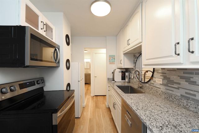 kitchen featuring appliances with stainless steel finishes, a sink, white cabinetry, tasteful backsplash, and light wood-type flooring