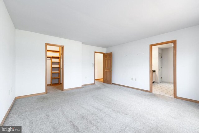unfurnished bedroom with a spacious closet, light carpet, baseboards, and a closet