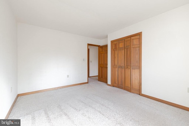 unfurnished bedroom featuring light carpet, a closet, and baseboards