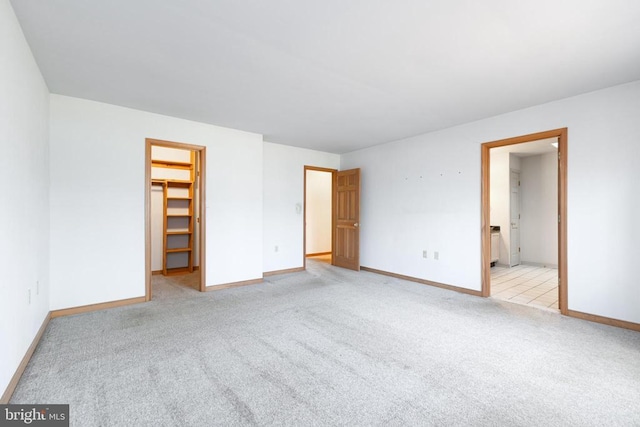 unfurnished bedroom featuring a spacious closet, light carpet, baseboards, and a closet